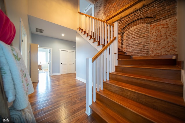 staircase featuring hardwood / wood-style flooring, brick wall, a high ceiling, visible vents, and baseboards