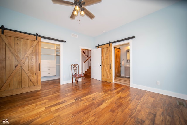 unfurnished bedroom featuring a barn door, wood finished floors, and visible vents