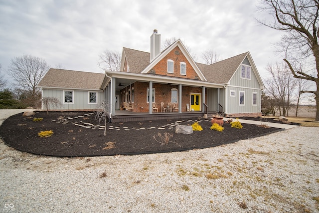 back of house featuring a porch, brick siding, a shingled roof, and a chimney