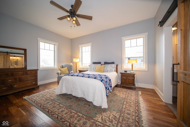 bedroom featuring ceiling fan, a barn door, wood finished floors, and baseboards