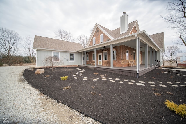 back of property with a ceiling fan, brick siding, a chimney, and roof with shingles