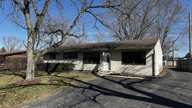 ranch-style home featuring a shingled roof, fence, and aphalt driveway