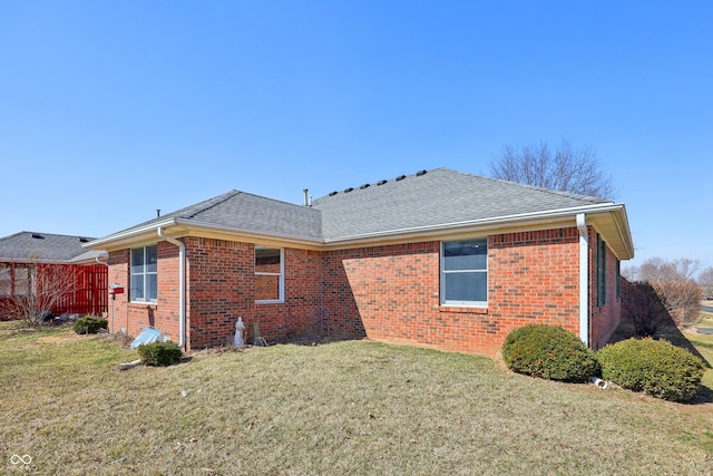 rear view of property with a lawn, brick siding, and roof with shingles