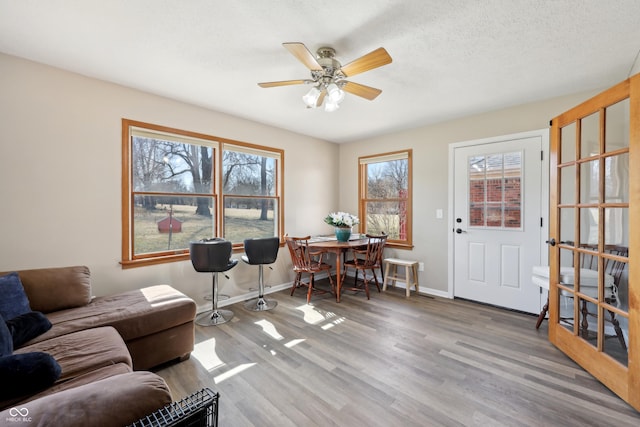 living area with ceiling fan, wood finished floors, baseboards, and a textured ceiling