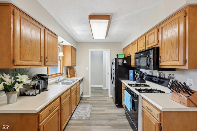 kitchen with black appliances, light countertops, light wood-style flooring, a textured ceiling, and a sink