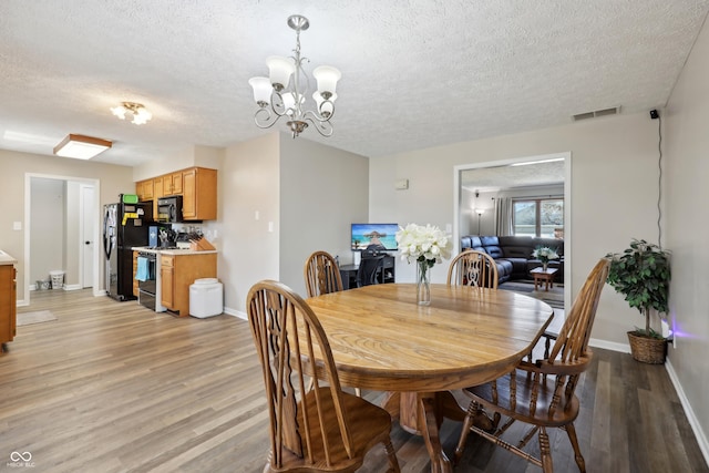 dining room featuring a chandelier, a textured ceiling, light wood-type flooring, and baseboards