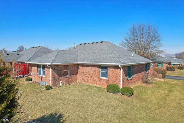 rear view of property featuring brick siding, a lawn, and roof with shingles