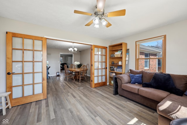 living area featuring ceiling fan with notable chandelier, french doors, baseboards, and wood finished floors