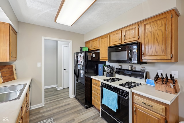 kitchen with black appliances, a sink, light wood-style floors, light countertops, and baseboards