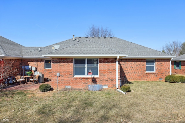 back of property with brick siding, roof with shingles, a lawn, crawl space, and a patio