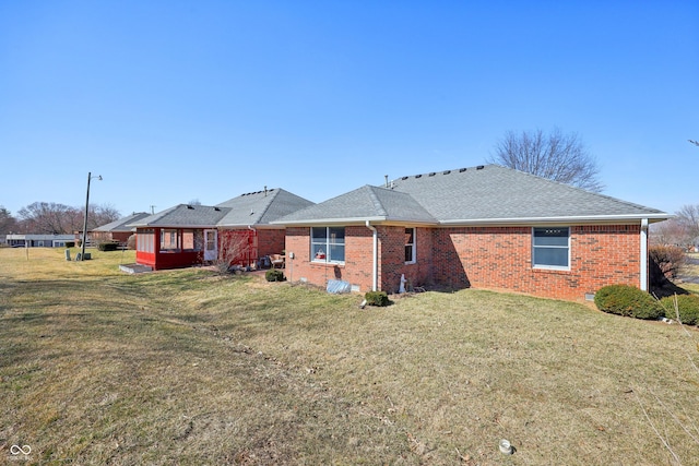 rear view of house featuring a yard, brick siding, and a shingled roof