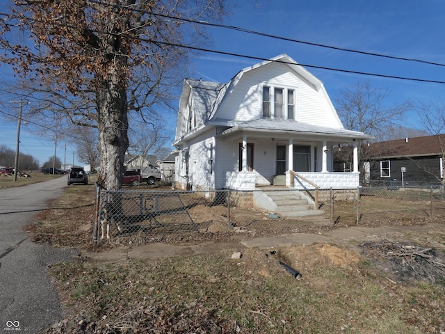 colonial inspired home with covered porch, a fenced front yard, and a gambrel roof