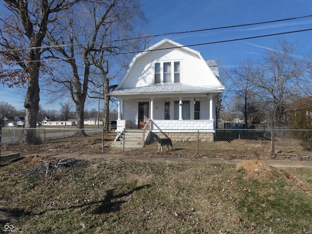 colonial inspired home featuring a porch, metal roof, a fenced front yard, and a gambrel roof