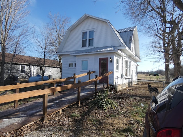 view of side of home featuring metal roof, a gambrel roof, and fence