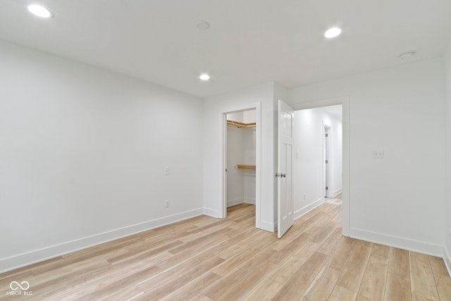 unfurnished bedroom featuring recessed lighting, light wood-type flooring, baseboards, and a walk in closet