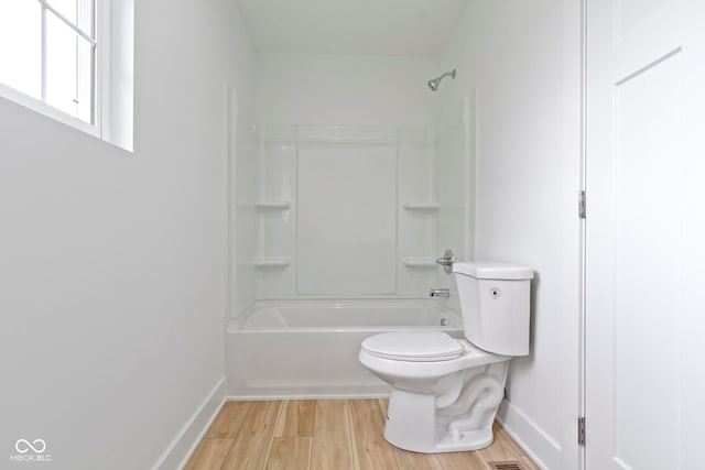 full bath with toilet, wood finished floors, baseboards, and shower / bathtub combination