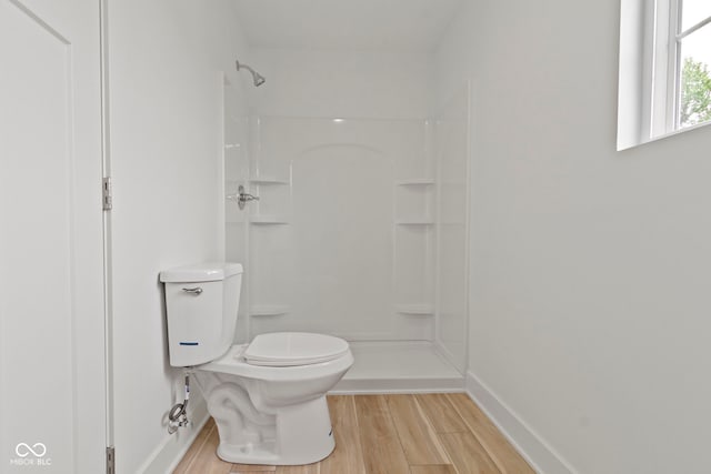 bathroom with toilet, wood finished floors, baseboards, and walk in shower