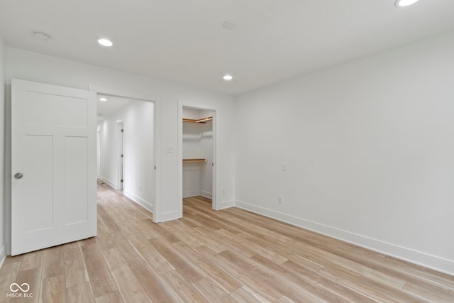 unfurnished bedroom featuring baseboards, recessed lighting, a closet, a walk in closet, and light wood-type flooring