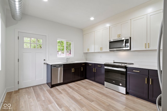 kitchen with light wood-type flooring, light countertops, appliances with stainless steel finishes, white cabinets, and a sink