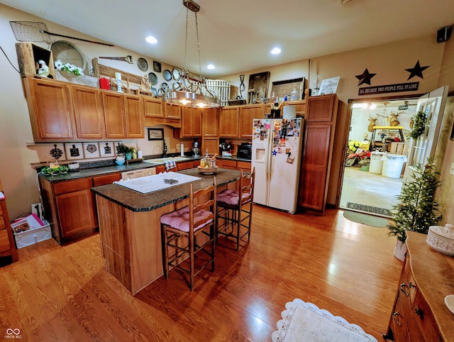 kitchen featuring light wood-type flooring, a kitchen bar, white refrigerator with ice dispenser, and a kitchen island