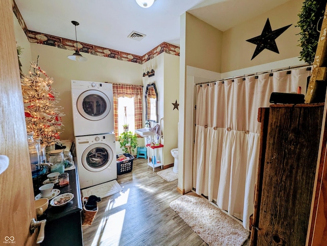 laundry area with laundry area, wood finished floors, visible vents, baseboards, and stacked washer / drying machine