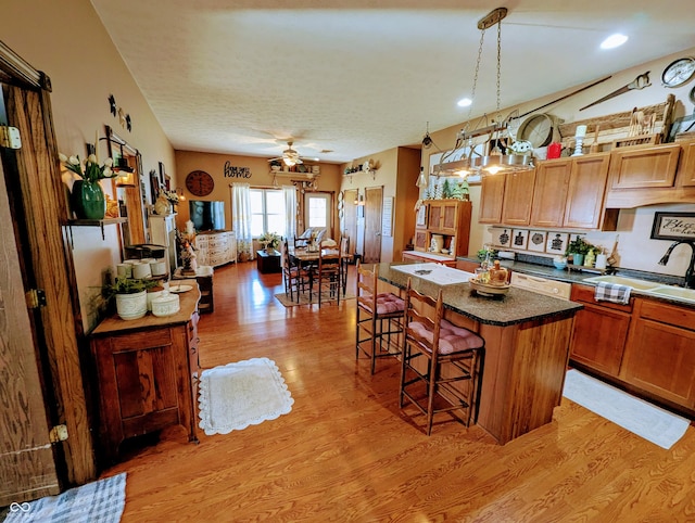 kitchen featuring a center island, dark countertops, light wood-style floors, a sink, and a kitchen bar