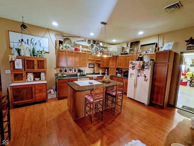 kitchen featuring visible vents, dark countertops, light wood-style flooring, a kitchen breakfast bar, and white fridge with ice dispenser