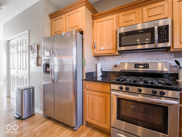 kitchen featuring stainless steel appliances, light wood finished floors, dark stone countertops, and tasteful backsplash