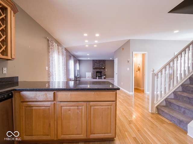 kitchen featuring a fireplace, open floor plan, light wood-type flooring, dishwasher, and dark stone countertops