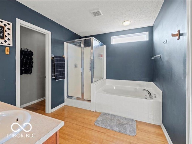 bathroom with wood finished floors, visible vents, a stall shower, a textured ceiling, and a garden tub