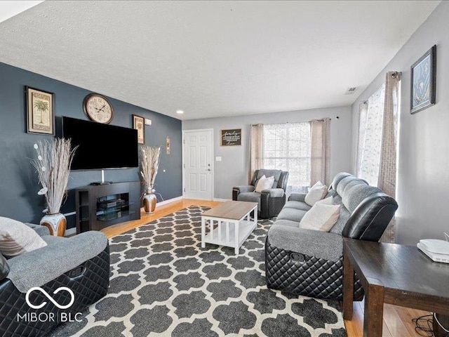 living area with visible vents, wood finished floors, baseboards, and a textured ceiling