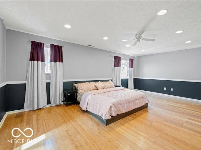 bedroom with ceiling fan, wood finished floors, visible vents, and a textured ceiling