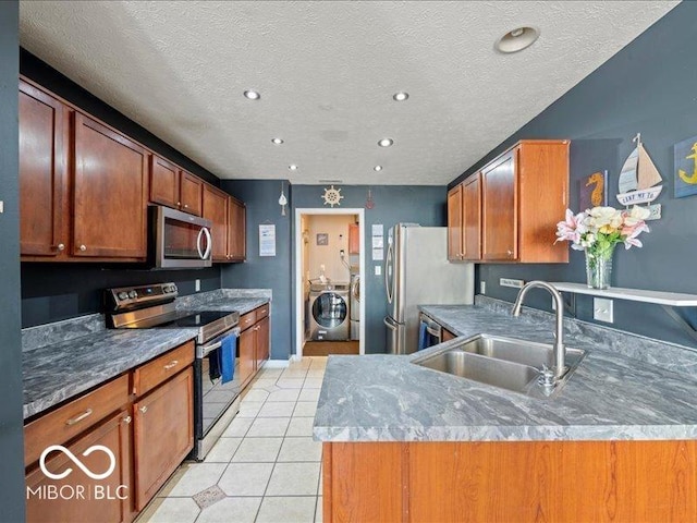 kitchen with a sink, stainless steel appliances, light tile patterned flooring, brown cabinetry, and washing machine and clothes dryer