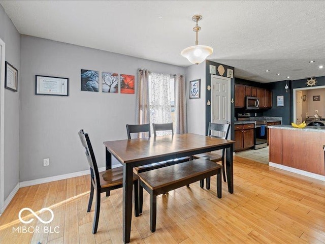 dining area with light wood-style flooring, baseboards, and a textured ceiling