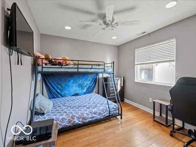 bedroom with visible vents, baseboards, wood finished floors, a textured ceiling, and a ceiling fan