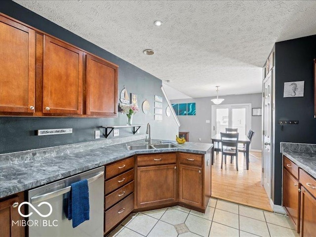 kitchen featuring a sink, stainless steel dishwasher, a peninsula, brown cabinetry, and light tile patterned floors