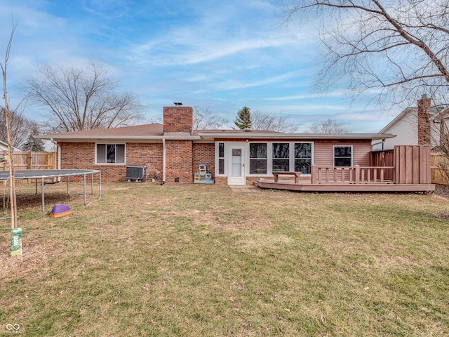 back of property with a trampoline, brick siding, a chimney, central AC unit, and fence