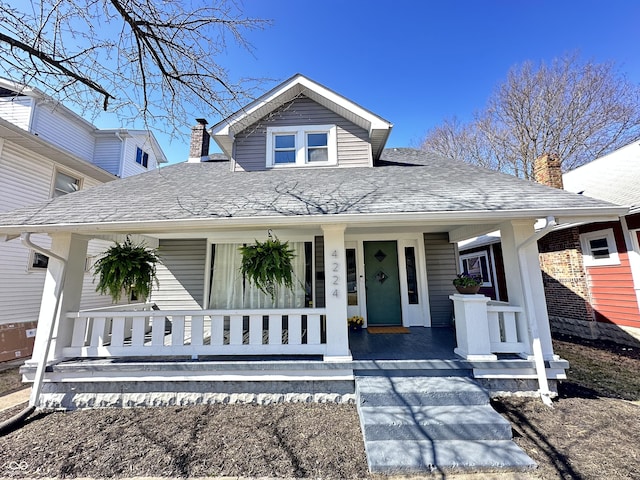 bungalow featuring covered porch, roof with shingles, and a chimney