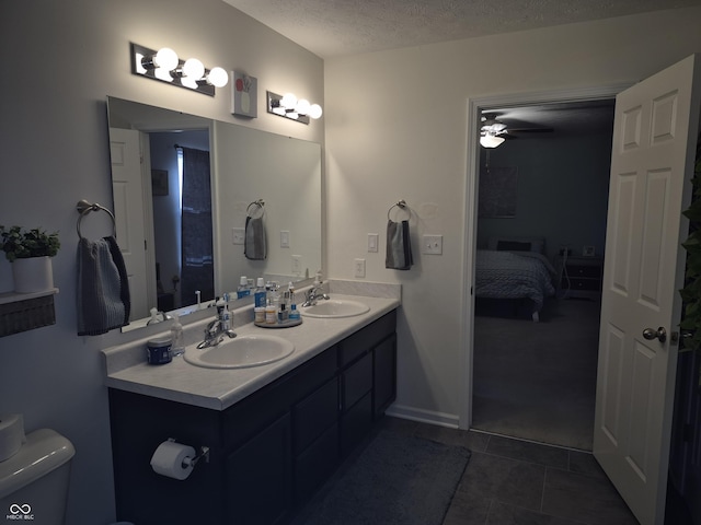 ensuite bathroom featuring toilet, a textured ceiling, a sink, and tile patterned floors