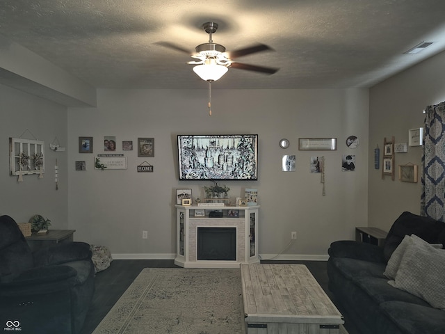 living area with a textured ceiling, ceiling fan, a fireplace, visible vents, and baseboards