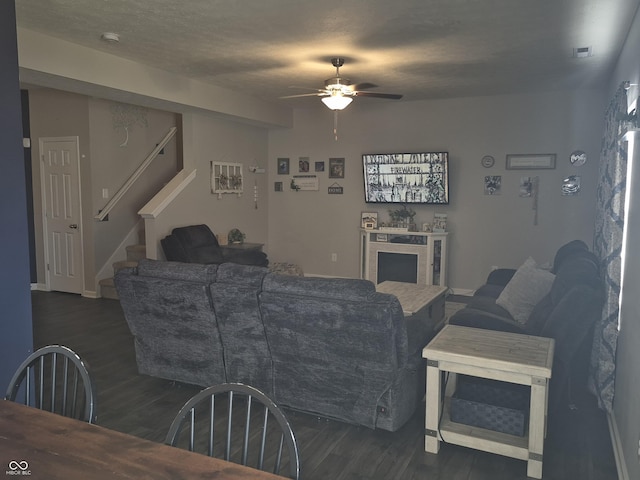 living area featuring dark wood-style floors, a ceiling fan, a textured ceiling, and stairs