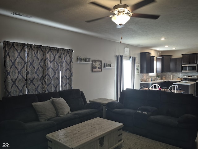 living room featuring a ceiling fan, visible vents, and a textured ceiling