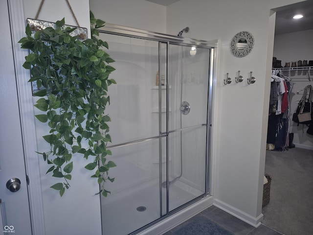 full bath with a stall shower, baseboards, a walk in closet, and tile patterned floors