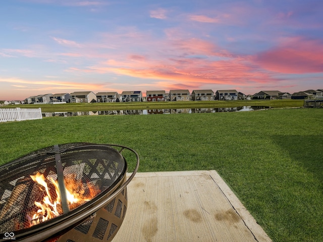 yard at dusk with a fire pit, a water view, fence, and a residential view