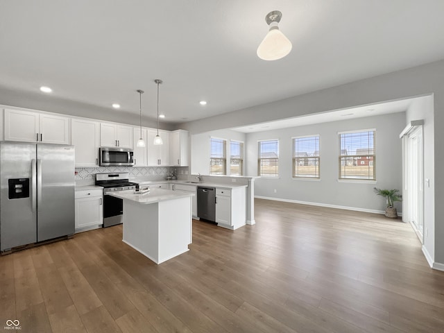 kitchen featuring appliances with stainless steel finishes, wood finished floors, a peninsula, light countertops, and a sink