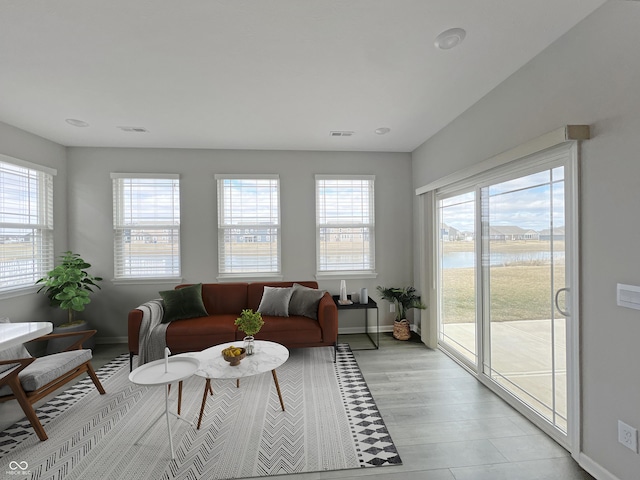 living room featuring light wood finished floors, a water view, visible vents, and baseboards