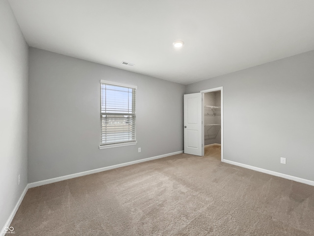 unfurnished bedroom featuring baseboards, visible vents, a walk in closet, and carpet flooring