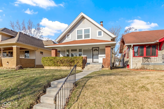 view of front of home featuring brick siding, covered porch, a chimney, and a front yard