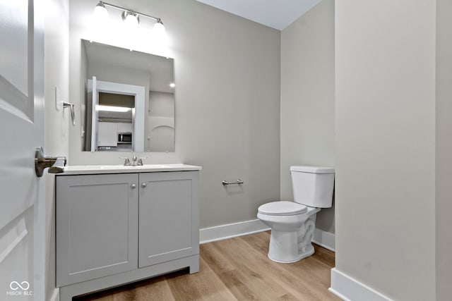 bathroom featuring baseboards, toilet, wood finished floors, and vanity