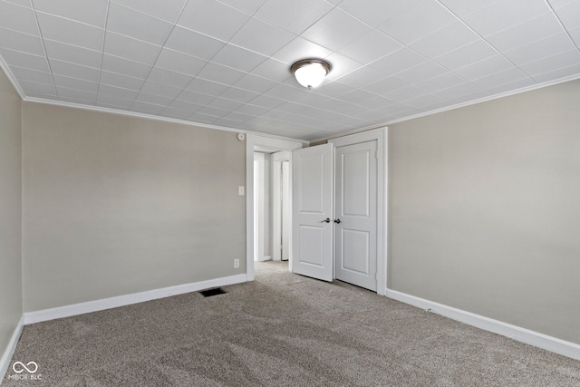 spare room featuring carpet flooring, visible vents, baseboards, and ornamental molding